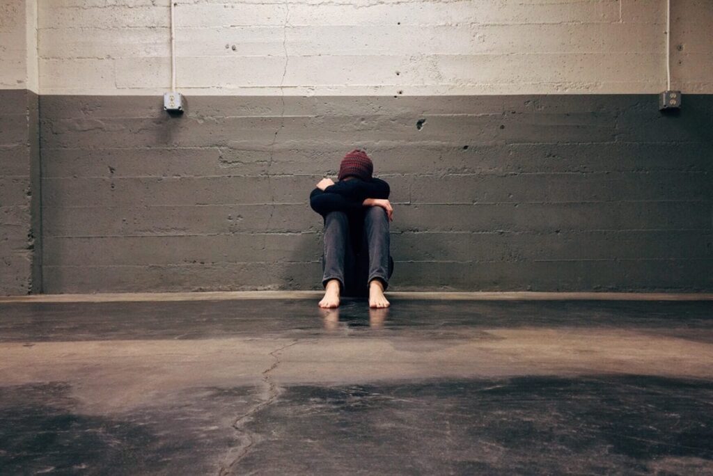 a person sits on the floor with their head on their knees